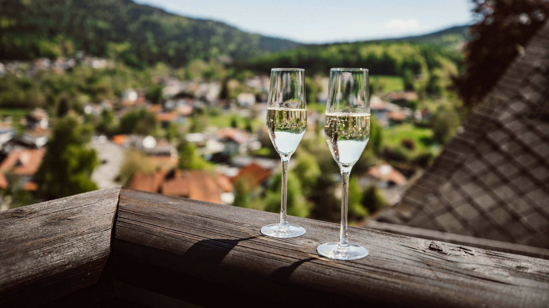 Ihr Traumurlaub im Hotel Hofbräuhaus Zwei Sektgläser auf dem Balkon mit Panoramablick über Bodenmais und den Bayerischen Wald – Genussmoment im Wellnesshotel Hofbräuhaus