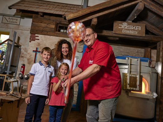 Wandern in Bodenmais: unsere Tipps Dieses Bild zeigt eine Familie in der Joska Glashütte, wo sie von einem Mitarbeiter in die Kunst des Glasblasens geführt werden.